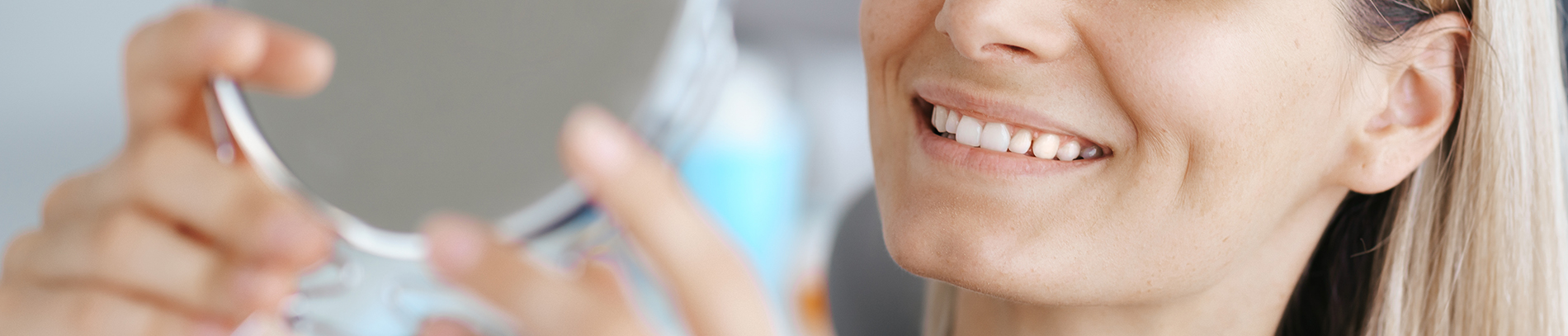 A person is seated in a dental chair, receiving care from a dental professional who stands behind them.